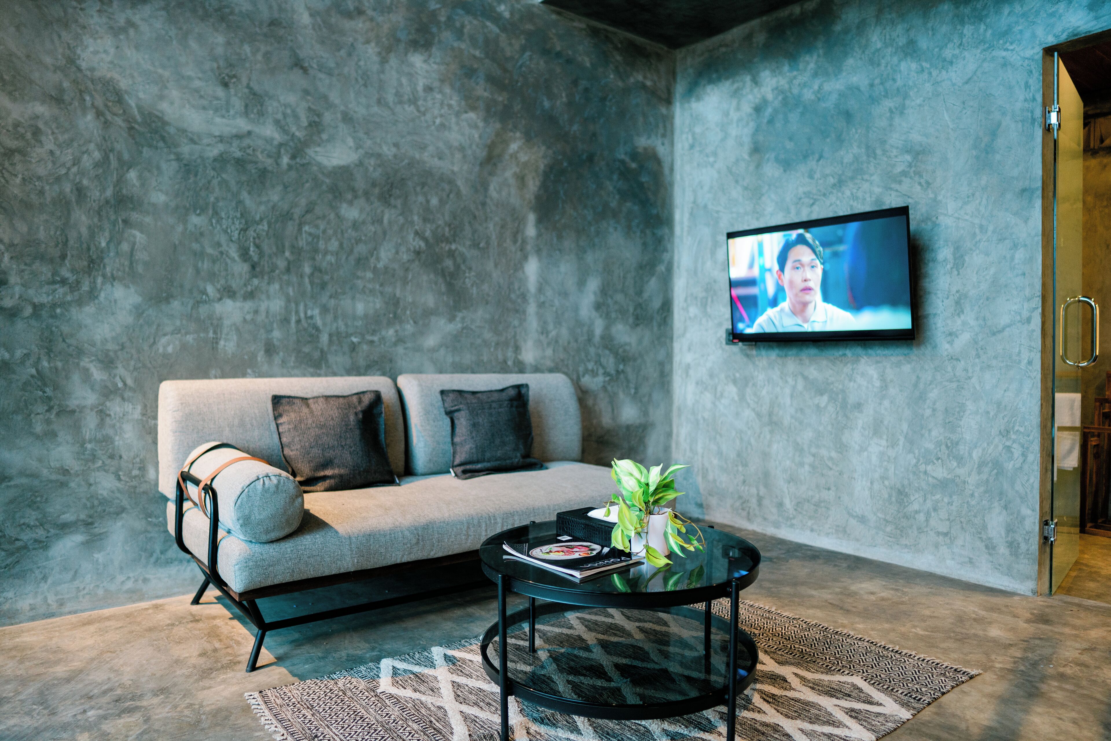 A modern living room with a grey sofa, a glass coffee table, and a flat-screen TV mounted on the wall.