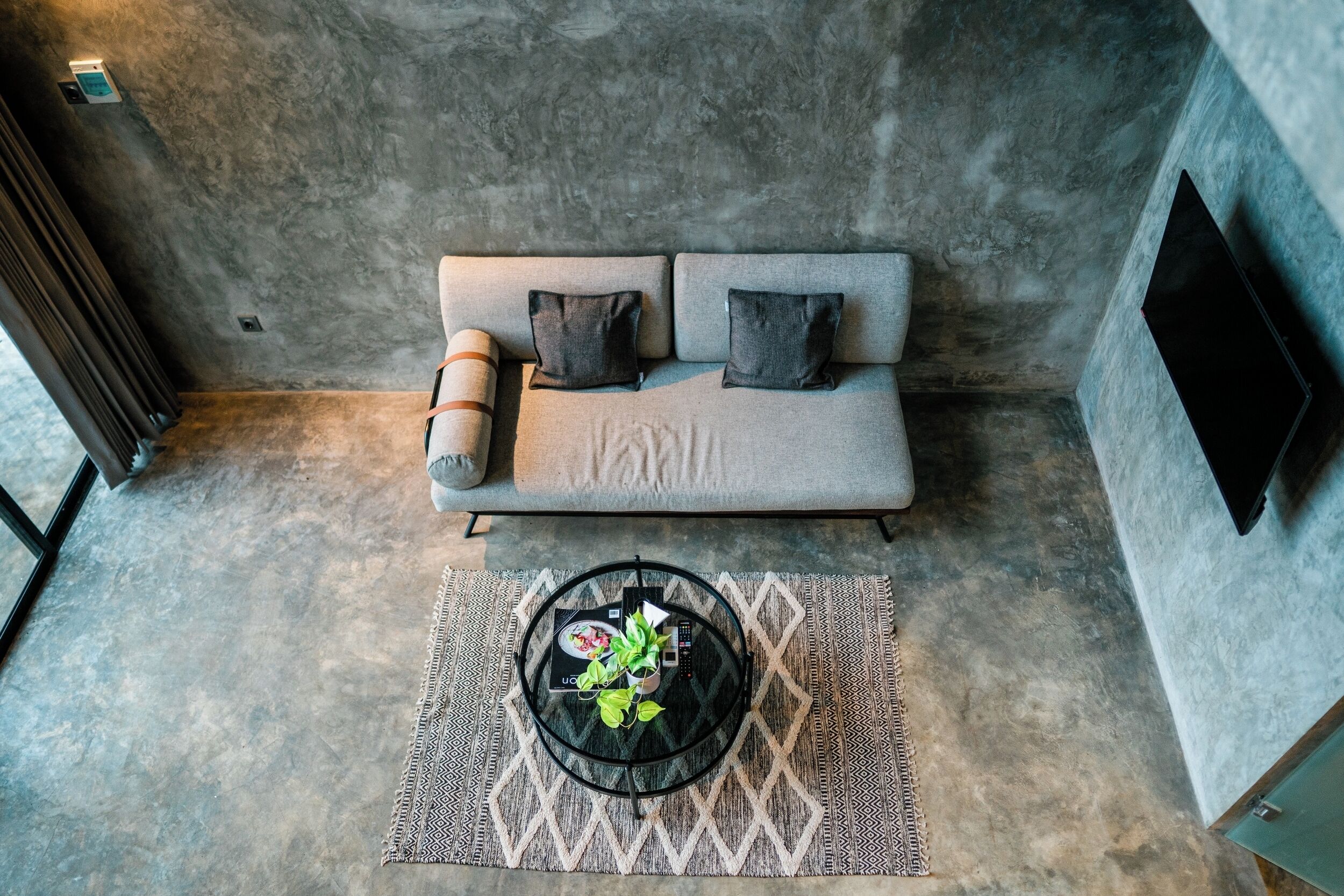 A modern living room with a sofa, a coffee table with a plant, and a patterned rug.