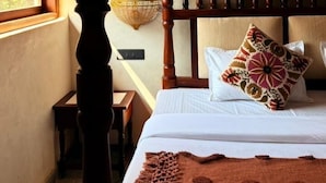 Un dormitorio con cama con dosel, una ventana con arco decorativo, una lámpara colgante y una mesita de noche.