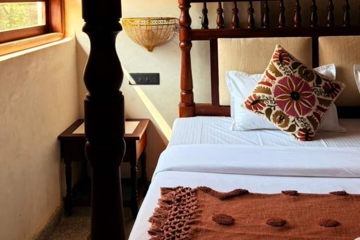 Un dormitorio con cama con dosel, una ventana con arco decorativo, una lámpara colgante y una mesita de noche.