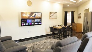 Ein modernes Wohnzimmer mit einem wandmontierten Flachbildfernseher, einem Essbereich mit Tisch und Stühlen sowie einer Küchenzeile mit Kühlschrank.