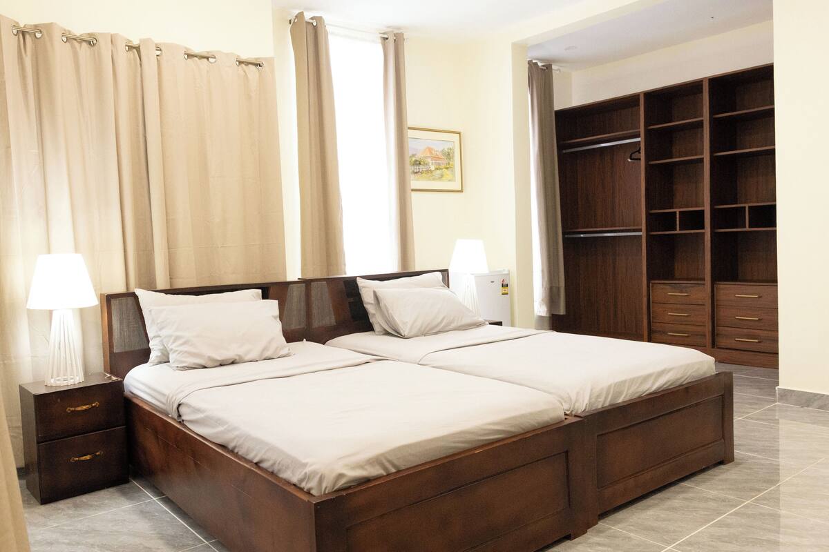 A double bed with a wooden frame, two bedside tables with lamps, a large wardrobe, and a painting on the wall.