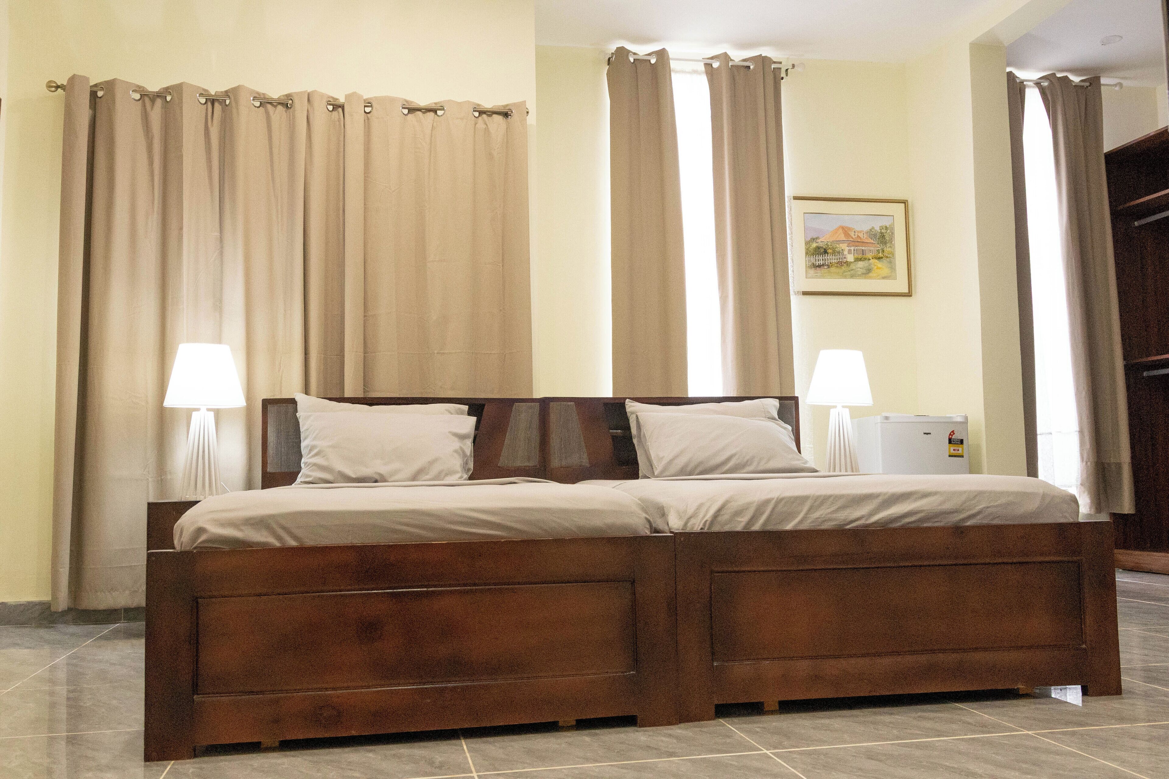 A double bed with a wooden frame, two bedside lamps, and beige curtains.