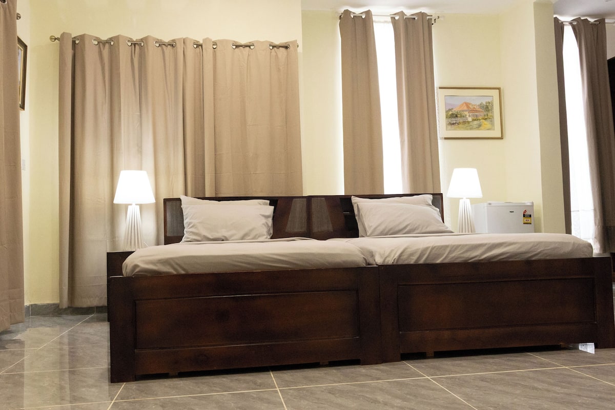 A double bed with a wooden frame, two bedside tables with lamps, beige curtains, and a framed picture on the wall.