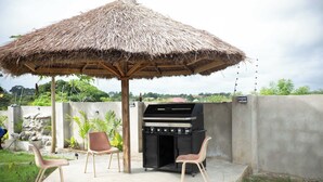 Eine Terrasse im Freien mit einem Reetdachschirm, einem Holzkohlegrill und zwei Stühlen.