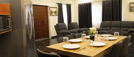 A dining area with a wooden table set for four, surrounded by black chairs, a refrigerator, and a wooden door.