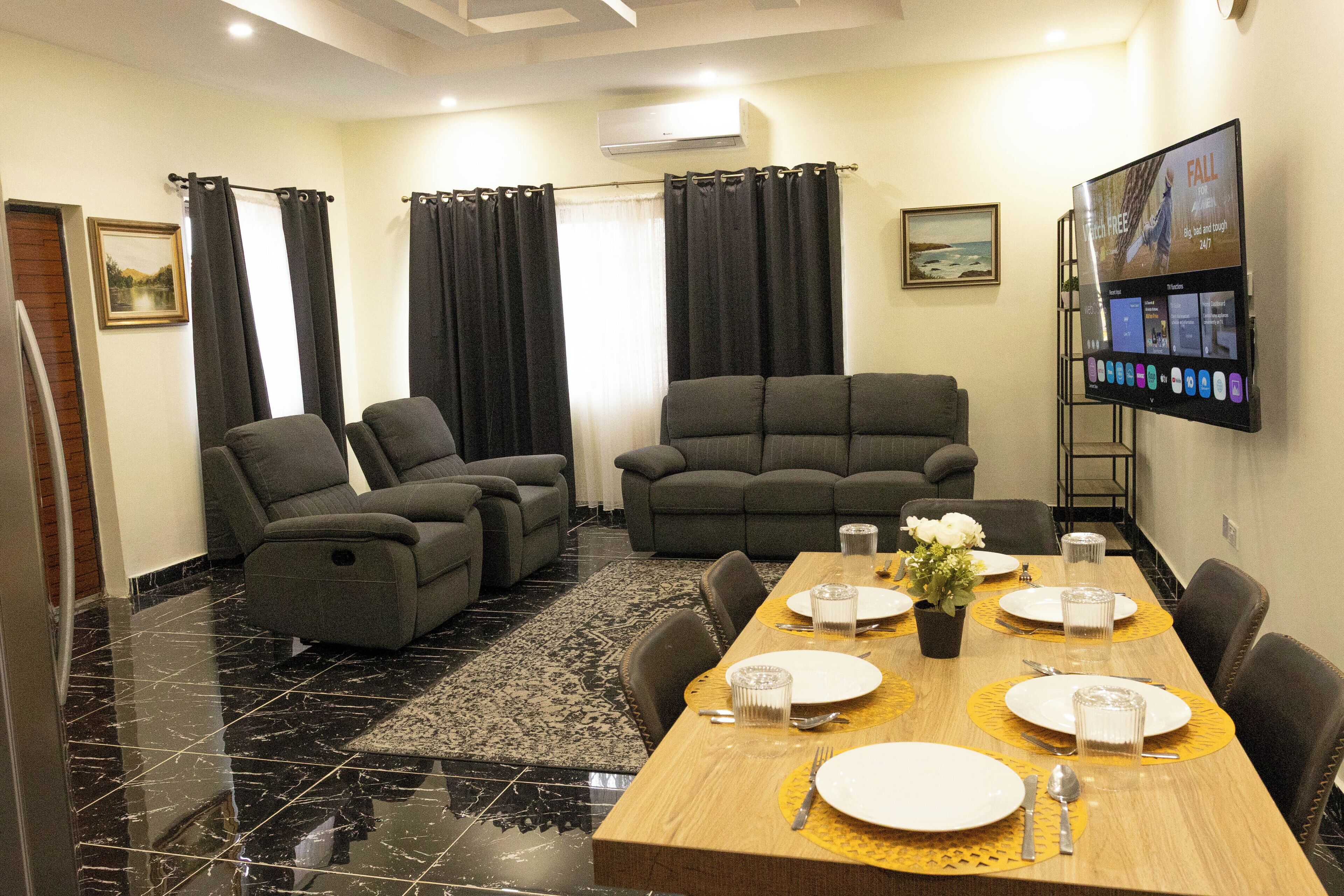 Un espace repas avec une table en bois dressée pour quatre personnes, entourée de canapés et de fauteuils gris.