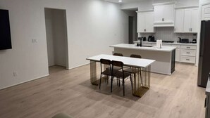 A modern kitchen with white cabinetry, a central island, and a dining area with a table and chairs. - Comfy gem (Richmond)