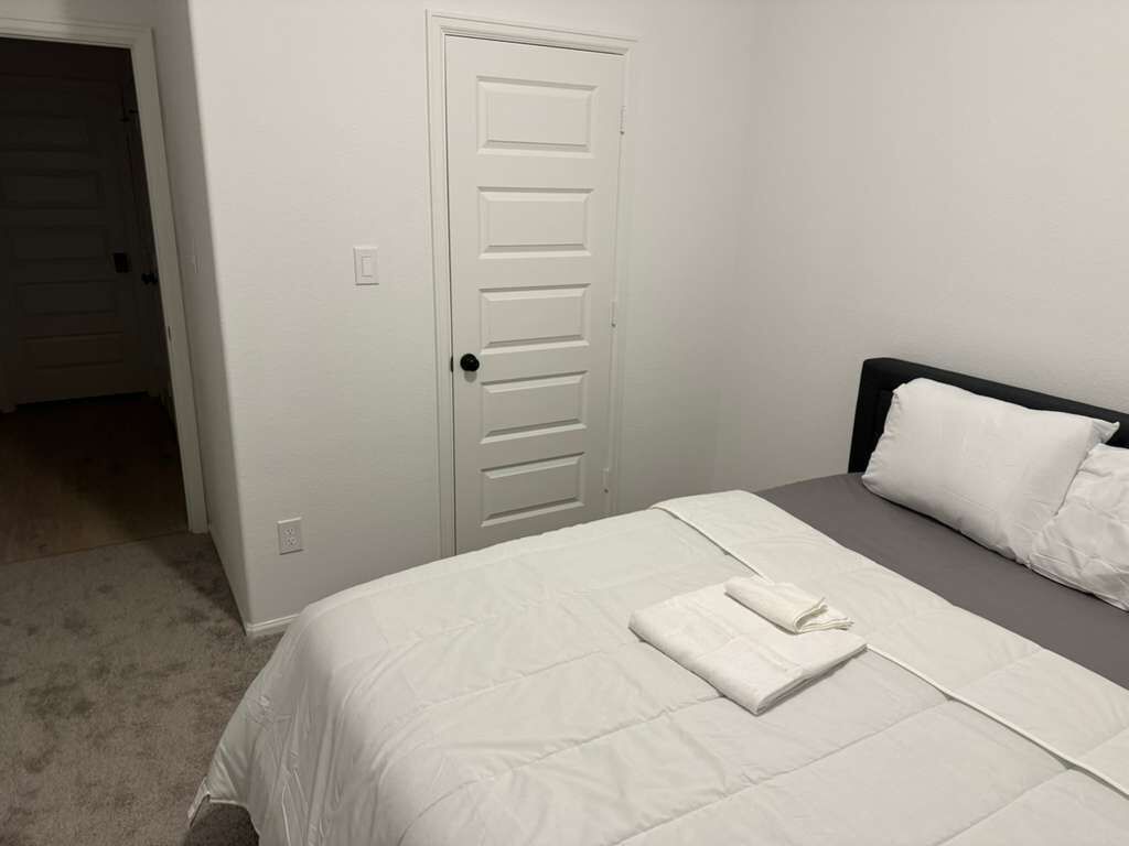 Un dormitorio con cama, una puerta y piso alfombrado.