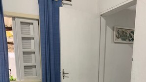 Makuuhuone, jossa on sänky, ikkuna, jossa on sälekaihtimet, ovi ja pieni taulu seinällä.