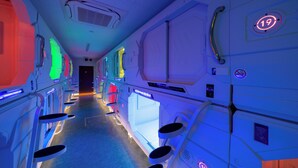 A futuristic hallway with illuminated walls, numbered doors, and a central walkway. - HB INN (Hiroshima)
