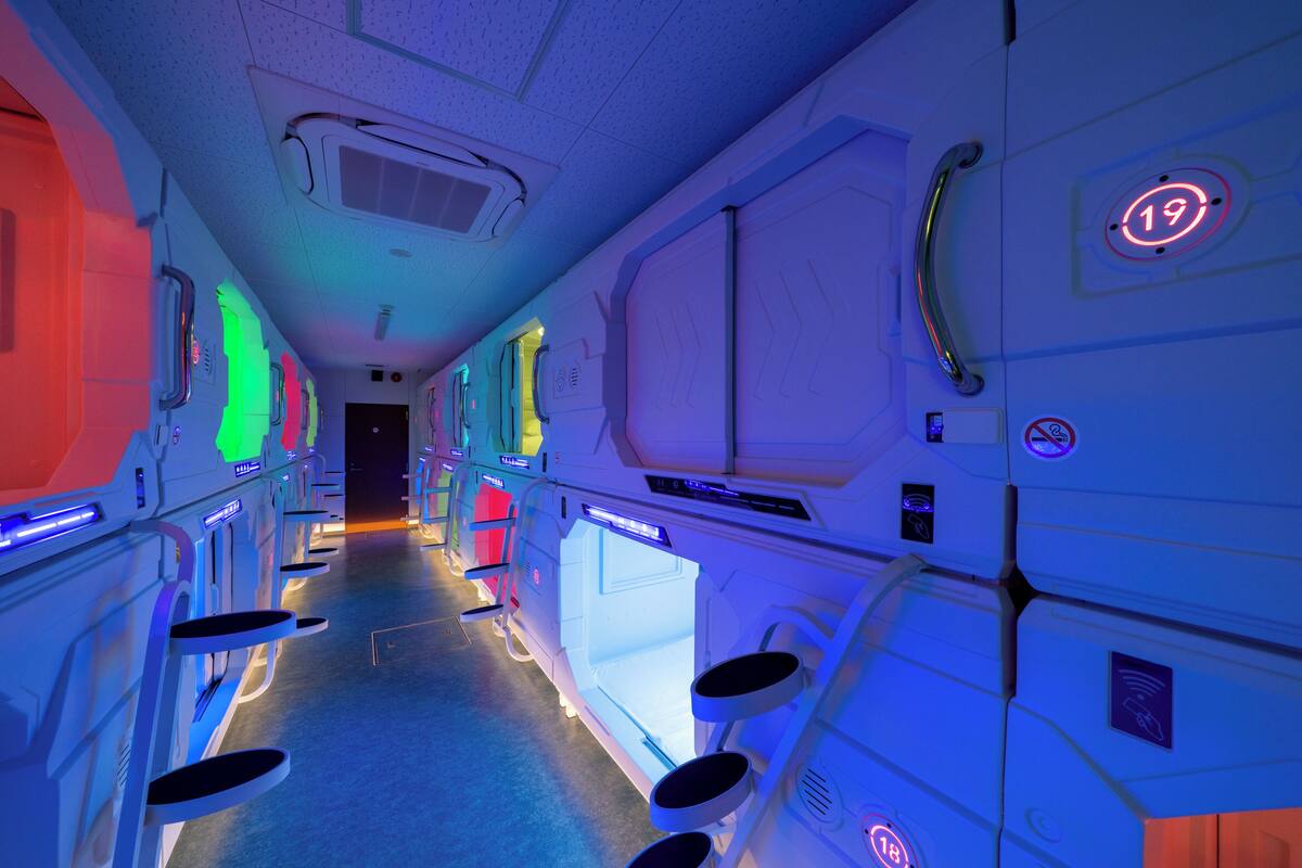 A futuristic hallway with illuminated walls, numbered doors, and a central walkway.