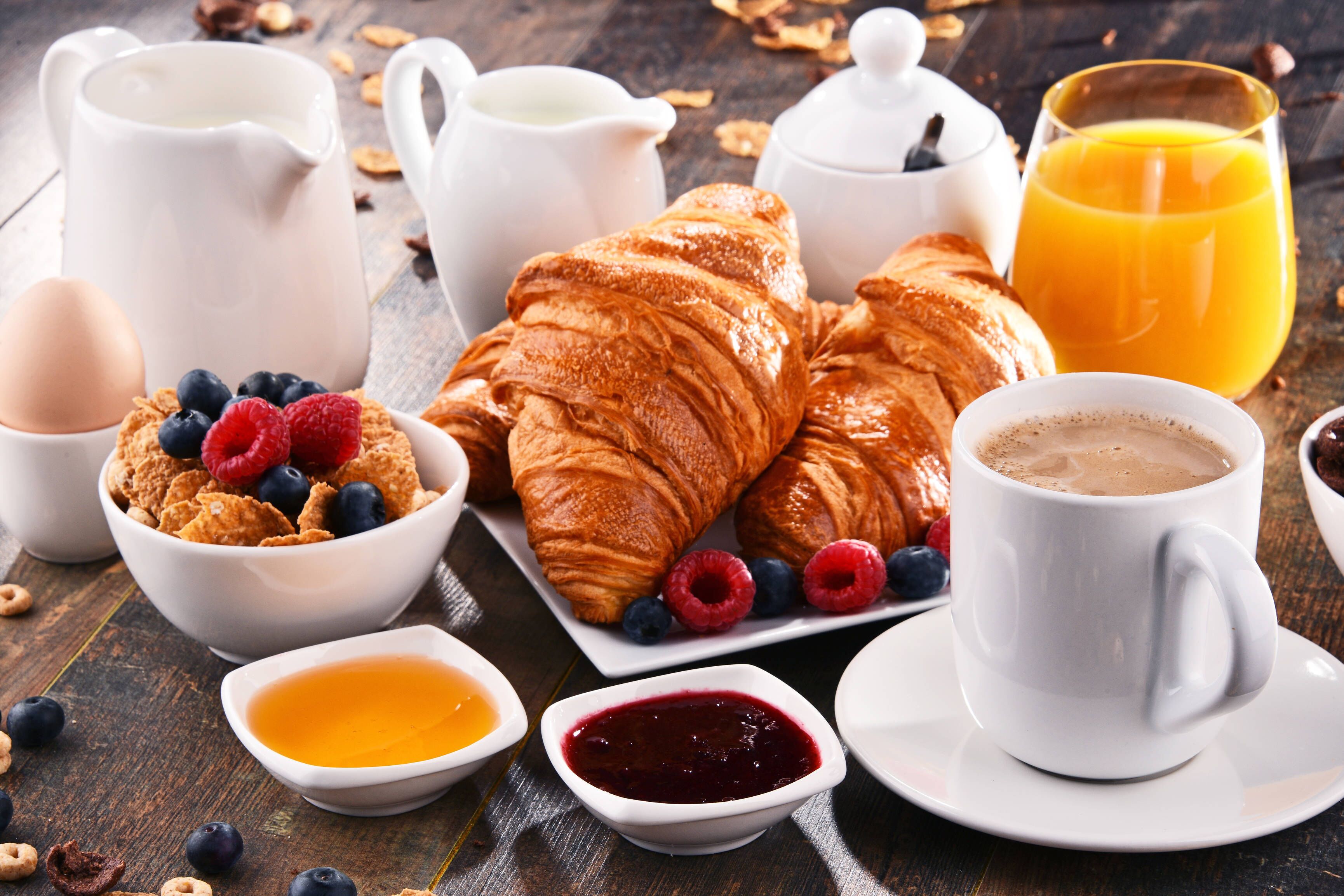 Une table de petit-déjeuner avec des croissants, des fruits rouges, des céréales, du café et du jus de fruits.