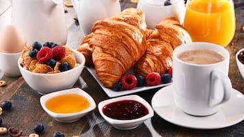 Une table de petit-déjeuner avec des croissants, des fruits rouges, des céréales, du café et du jus de fruits.