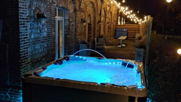 Un bain à remous doté d’un éclairage bleu, entouré d’un mur de briques et illuminé de guirlandes lumineuses.