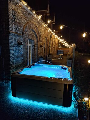 A hot tub with blue lighting, surrounded by a brick wall and string lights. - Le Clos Saint Vincent & SPA (Manneville-ès-Plains)