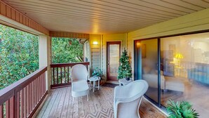 Eine überdachte Veranda mit Holzbalkonen, zwei Korbstühle, ein kleiner Tisch, ein Weihnachtsbaum und eine Glastür, die in einen Wohnbereich führt.