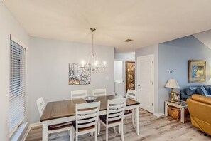 Een eetruimte met een houten tafel en witte stoelen, een kroonluchter en een schilderij aan de muur.