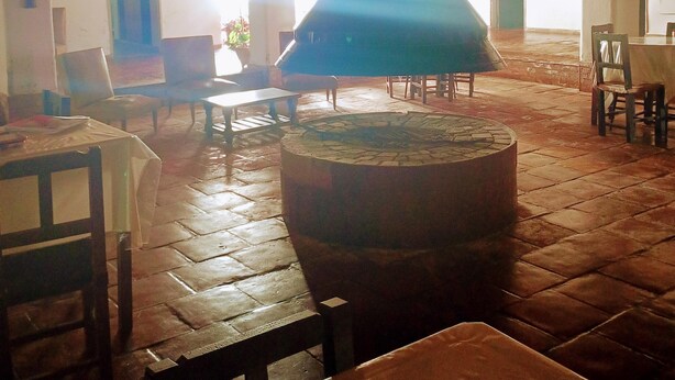A spacious room with a large central chimney, wooden flooring, and several tables and chairs. - Hotel Asembal (Cafayate)