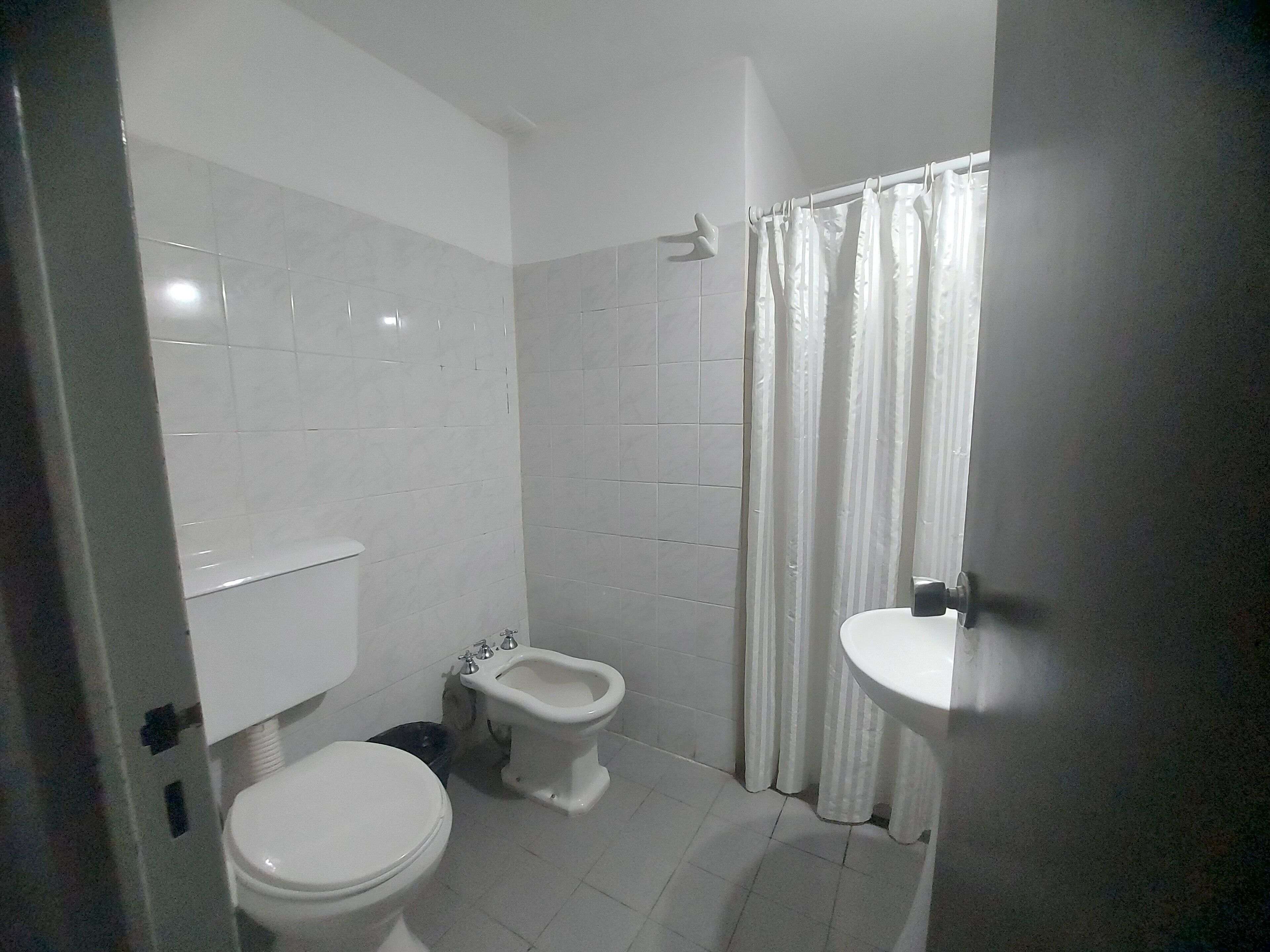 Een kleine, schone badkamer met witte tegels, een toilet, een bidet en een wastafel.