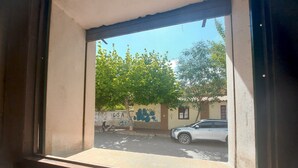 A window view of a street with a parked car, a motorcycle, and a tree. - Hotel Asembal (Cafayate)