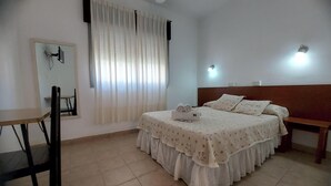 A bedroom with a bed, a bedside table, a chair, a mirror, and a window with curtains. - Hotel Asembal (Cafayate)