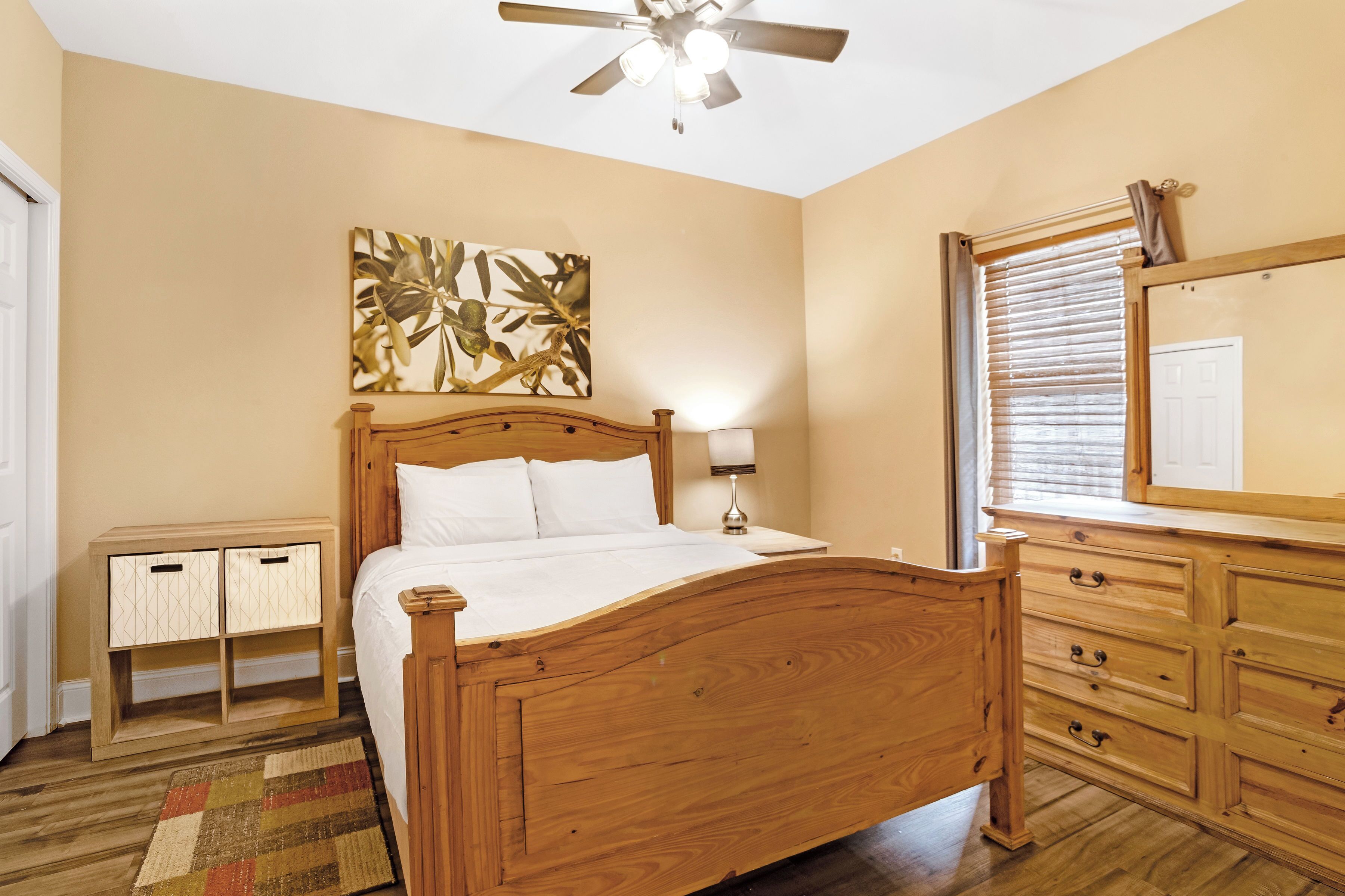 A bedroom with a wooden bed, a nightstand, a dresser, a ceiling fan, and a large mirror.