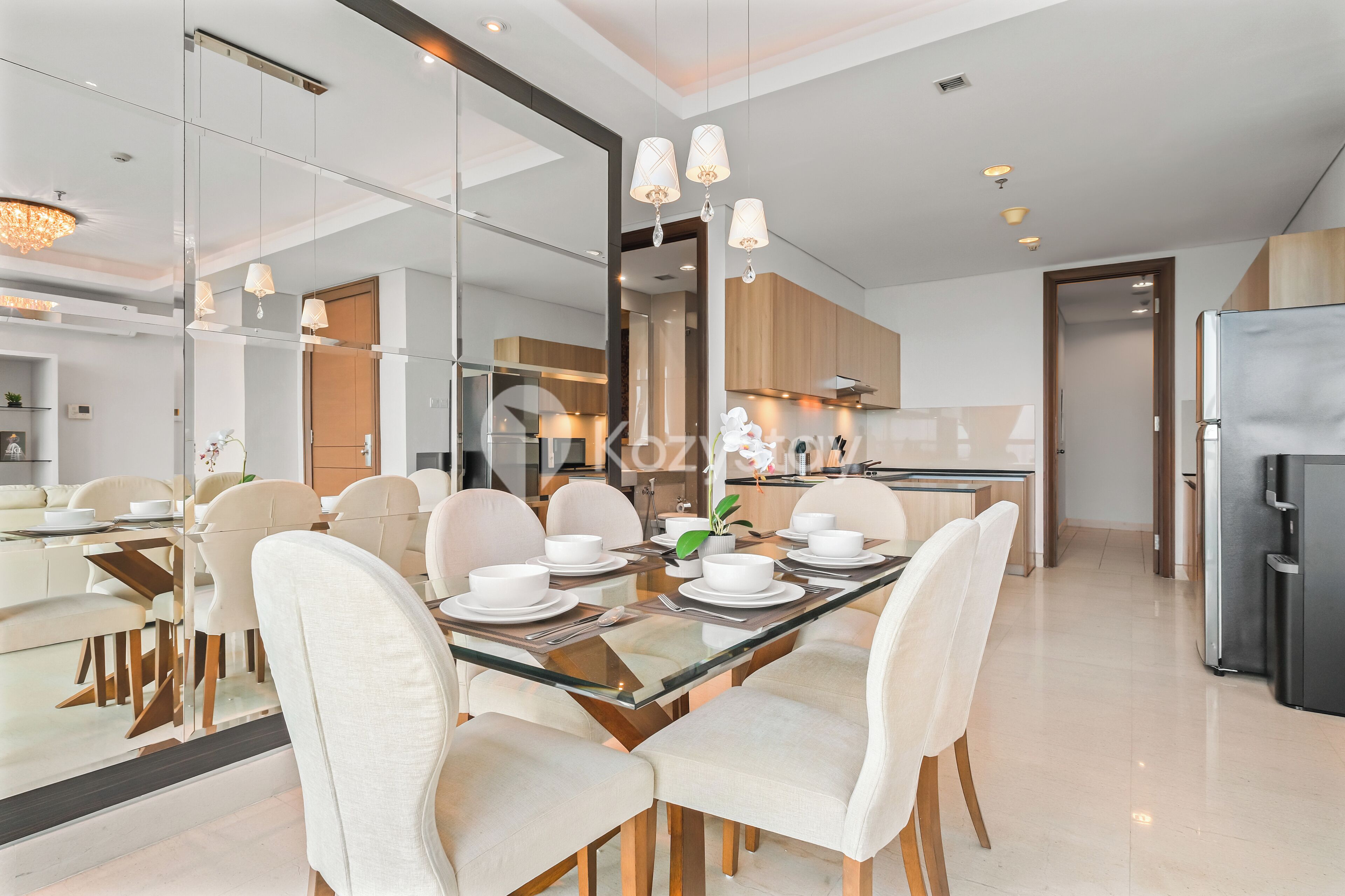 Uma sala de jantar moderna com mesa de vidro, cadeiras brancas e um lustre.