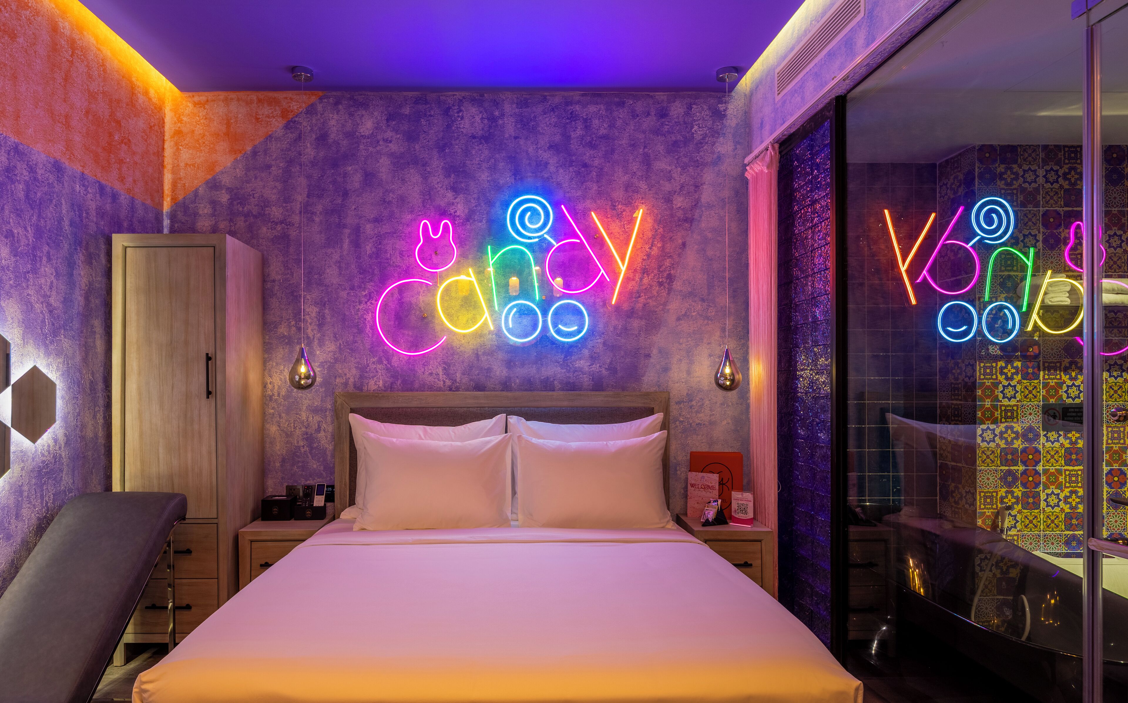A modern hotel room with a bed, a nightstand, a wardrobe, and neon signs on the wall.