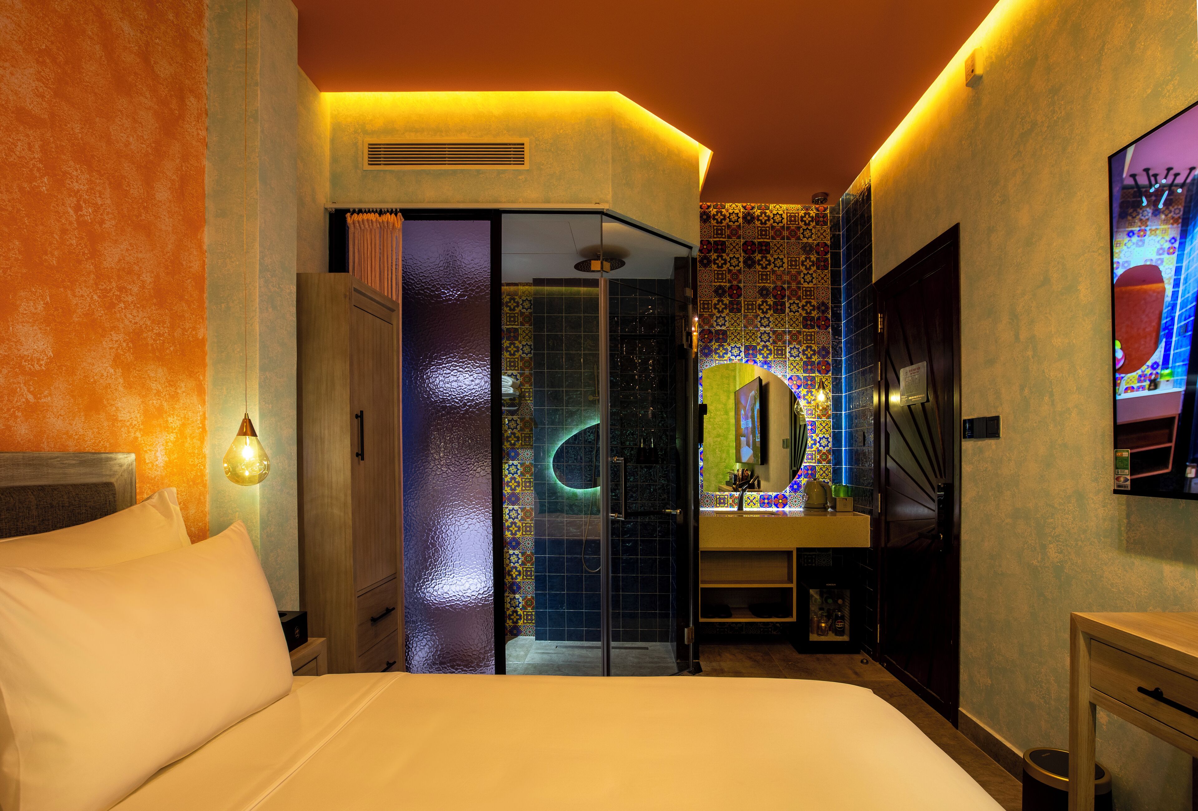A hotel room with a bed, a bathroom with a shower, and a TV mounted on the wall.
