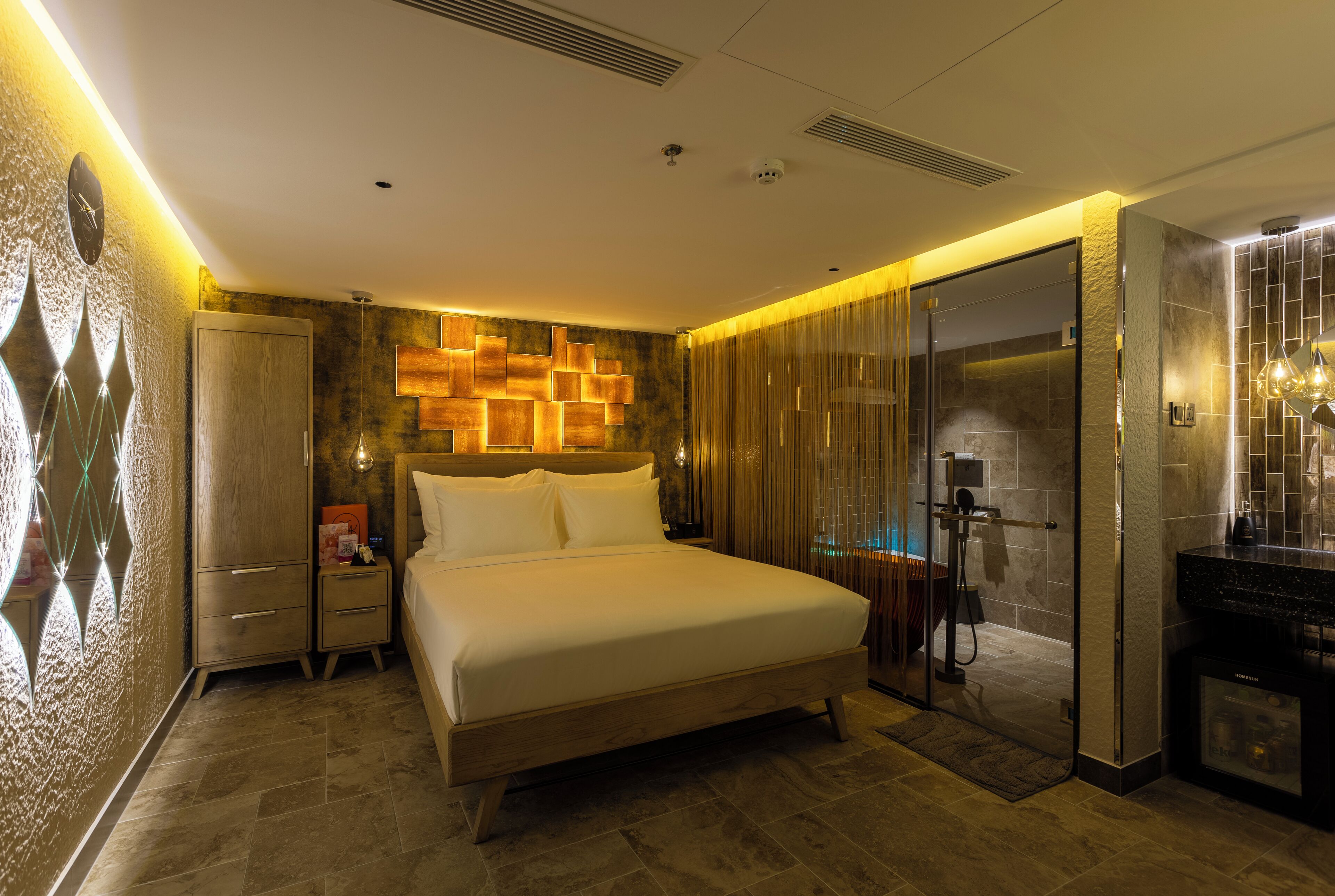 Een moderne hotelkamer met een groot bed, een kledingkast, een kaptafel met spiegel en een douche.