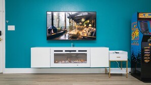 Eine türkisblaue Wand mit einem Flachbildfernseher, eine weiße Unterhaltungseinheit mit Kamin und eine Pac-Man-Spielmaschine.