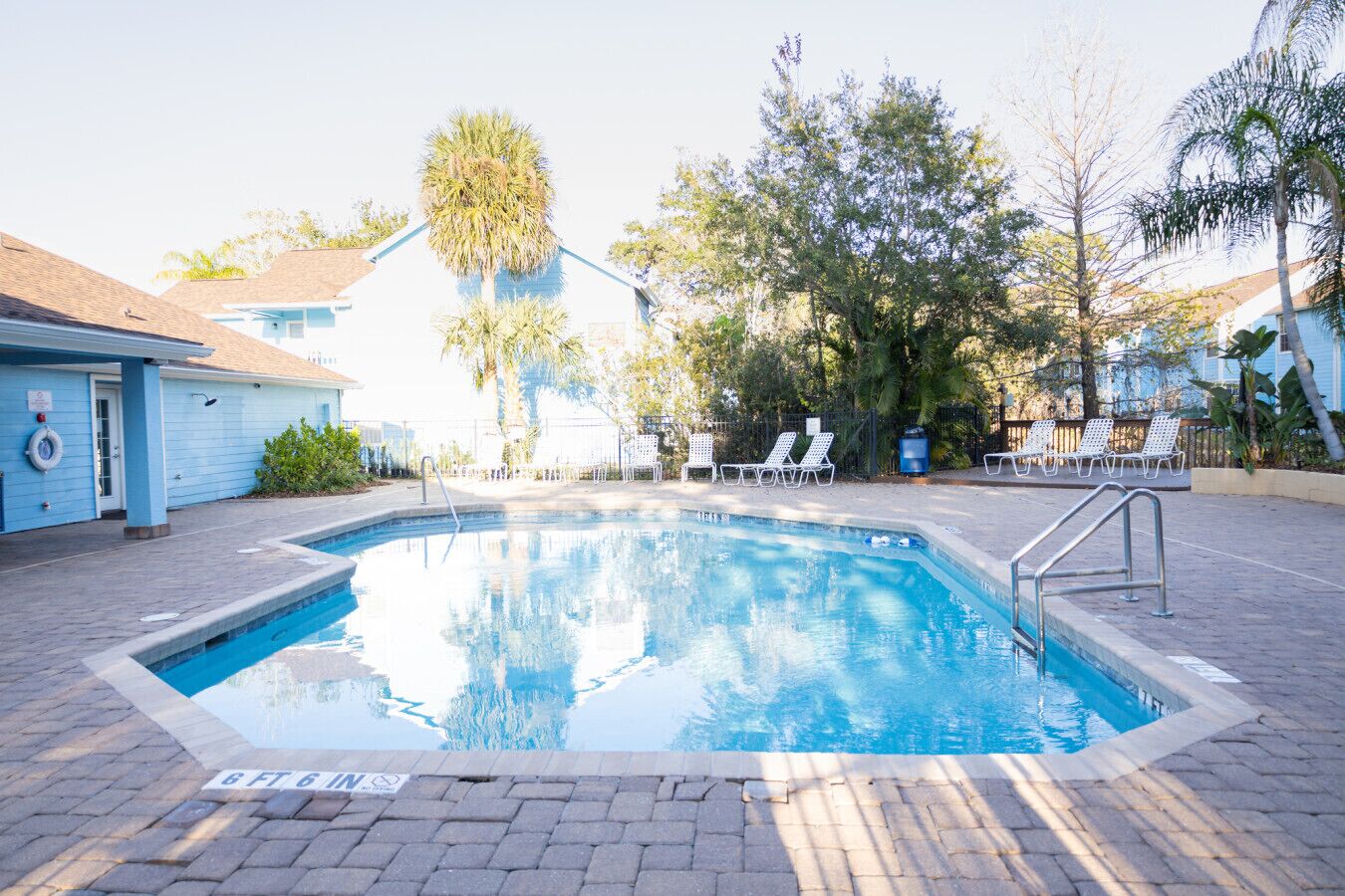A swimming pool with lounge chairs, a lifeguard stand, and a building in the background.