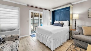 A bedroom with a large bed, a dresser, a chair, and a view of the outside. - Inlet Sands 105 (Panama City Beach)