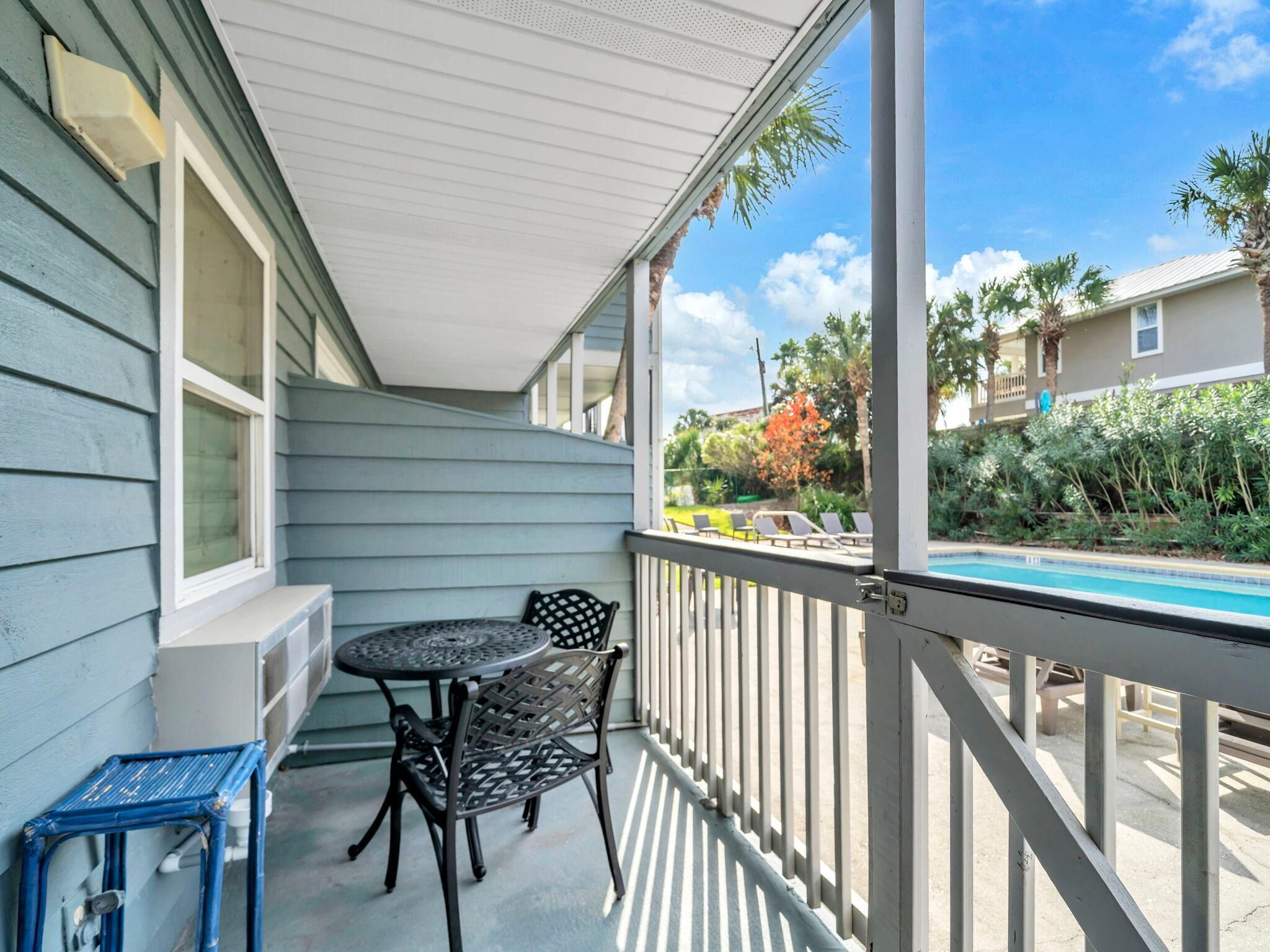 A covered outdoor area with a table and chairs, a pool in the background, and a view of neighboring houses.