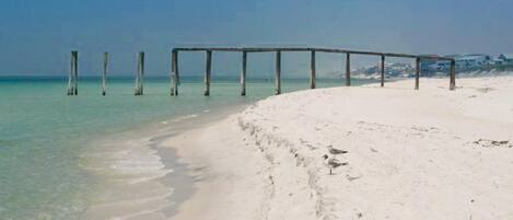 A beach with a wooden pier extending into the ocean, sandy shore, and a clear sky.