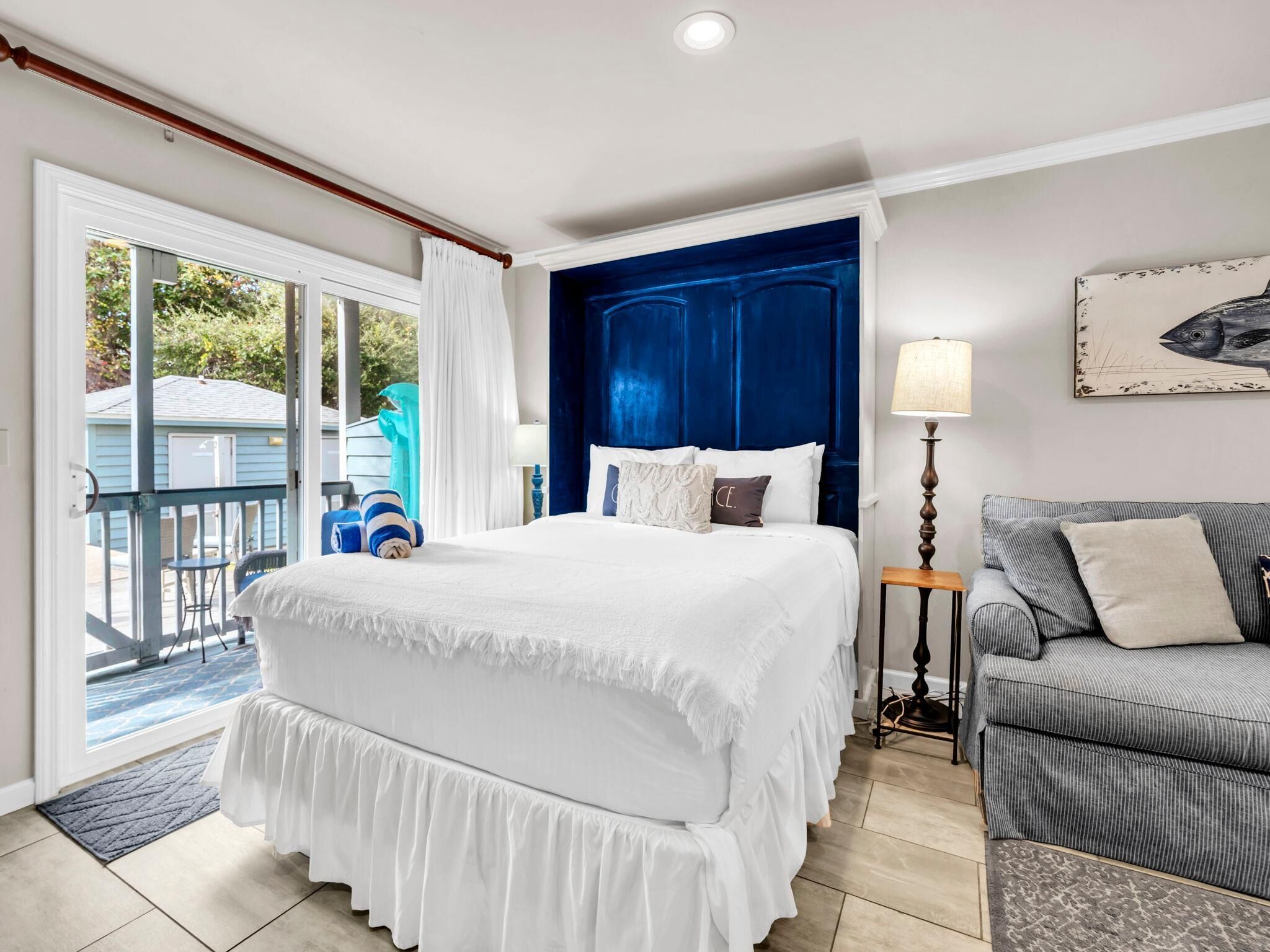 A hotel room with a bed, a gray sofa, a lamp, and a painting on the wall.