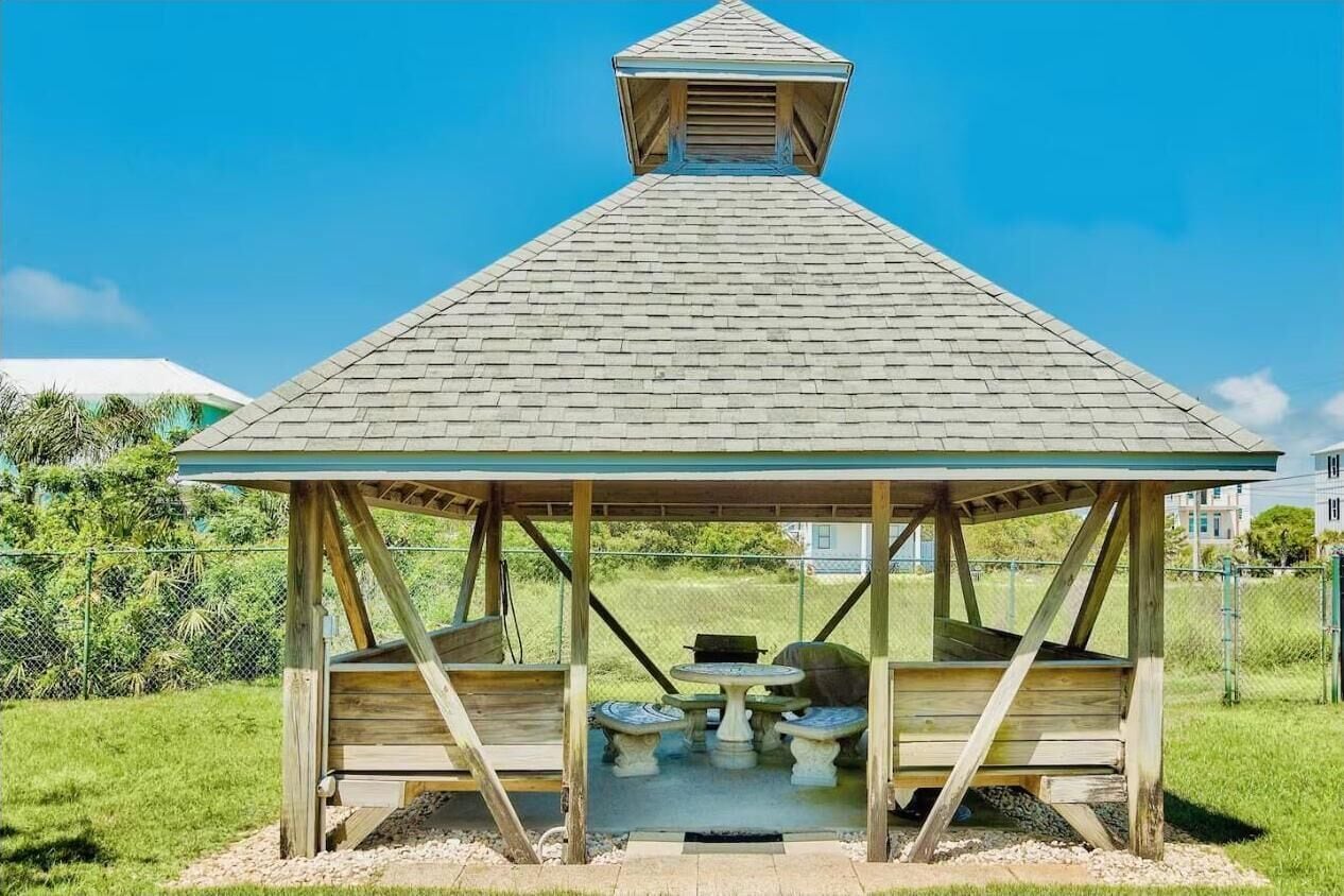 Una pérgola con techo inclinado y una pequeña ventana en la parte superior. Posee estructura de madera y está sostenida por cuatro patas.