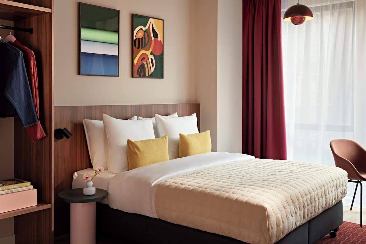 A neatly arranged bedroom with a bed, pillows, a nightstand, a chair, and artwork on the wall.