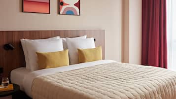 Una habitación de hotel con cama, almohadas, mesita de noche, lámpara y obras de arte en la pared.