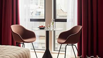 Una habitación de hotel moderna con un ventanal grande, dos sillas, una mesa redonda y una cama.