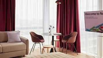 A hotel room with a bed, a sofa, two chairs, a small table, and a large window with curtains.