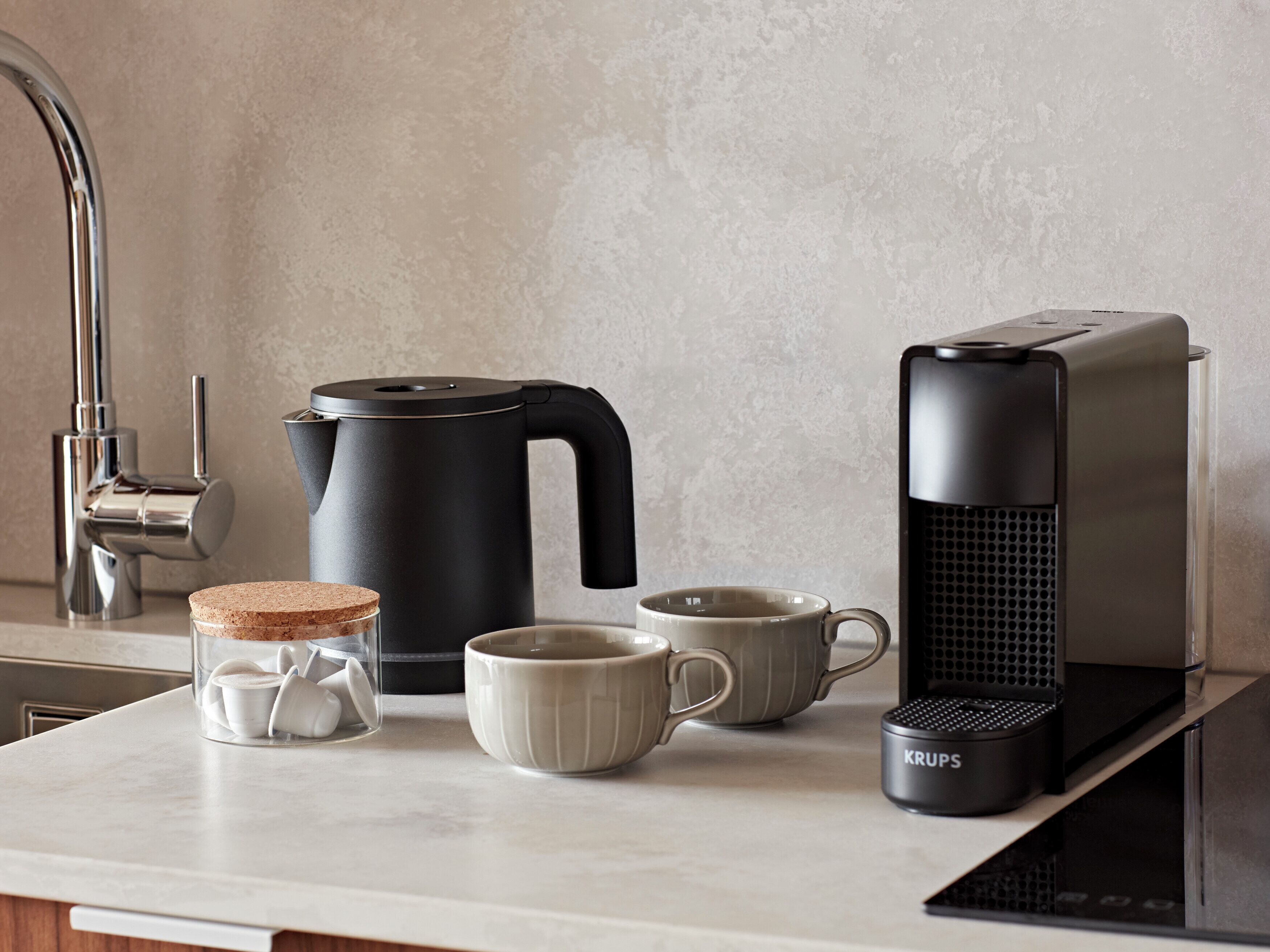 A kitchen with a coffee maker, kettle, mug, and a Krups coffee grinder on the counter.