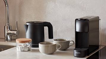 A kitchen with a coffee maker, kettle, mug, and a Krups coffee grinder on the counter.