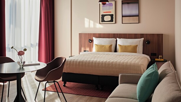 Ein modernes Hotelzimmer mit Bett, einer Couch, einem Esstisch mit Stühlen, einer Vase mit Blumen und Bildern an der Wand.