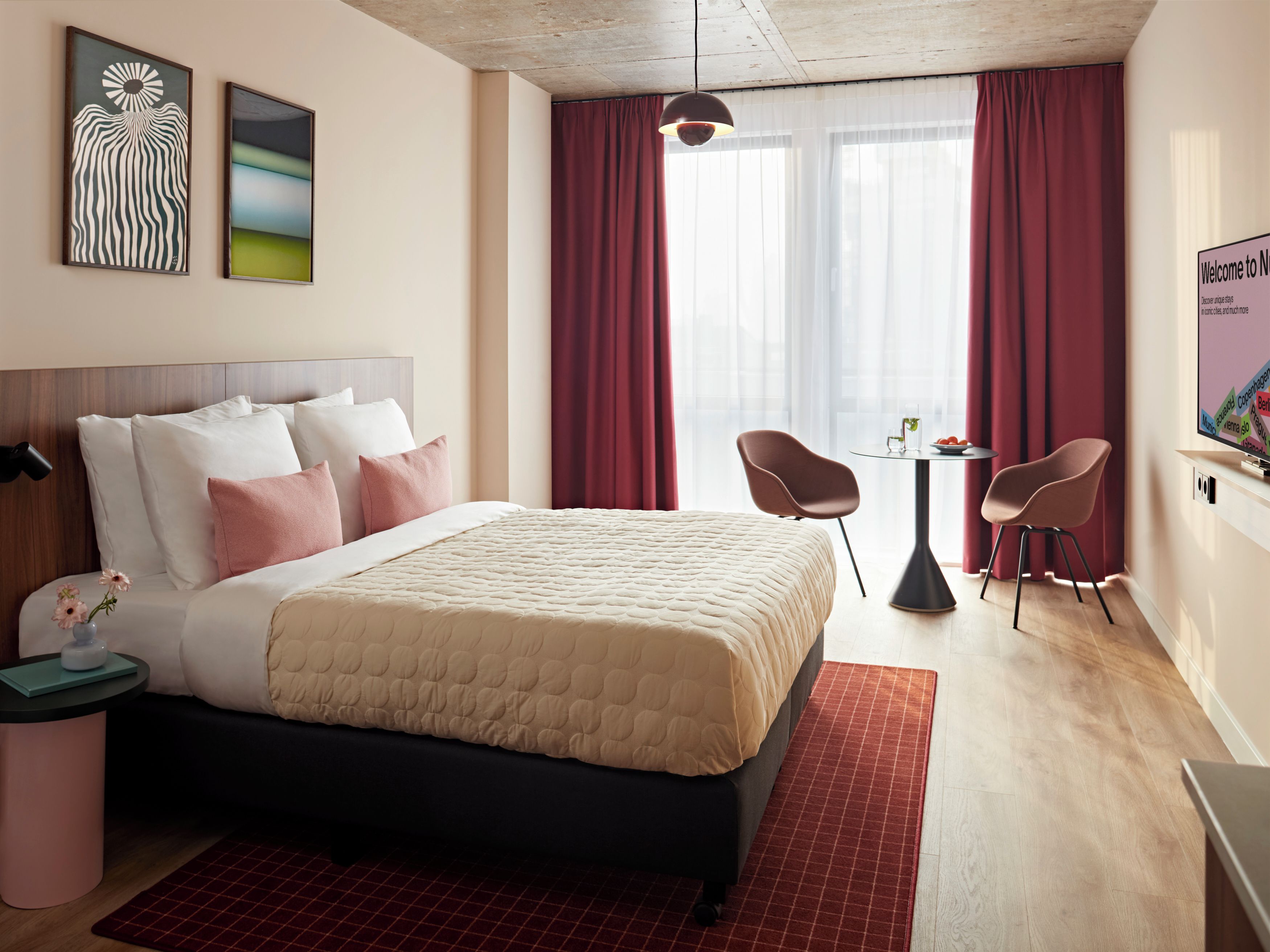 A hotel room with a bed, two chairs, a small table, a TV, and artwork on the wall.