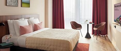 Ein Hotelzimmer mit einem Bett, zwei Sesseln, einem kleinen Tisch, einem Fernseher und Bildern an der Wand.