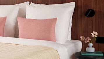 A neatly made bed with white and pink pillows, a beige quilt, and a small bedside table with a vase of flowers.