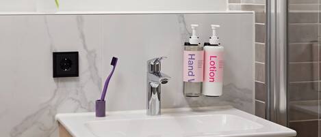 A bathroom with a white sink, a purple toothbrush holder, and two bottles of lotion.
