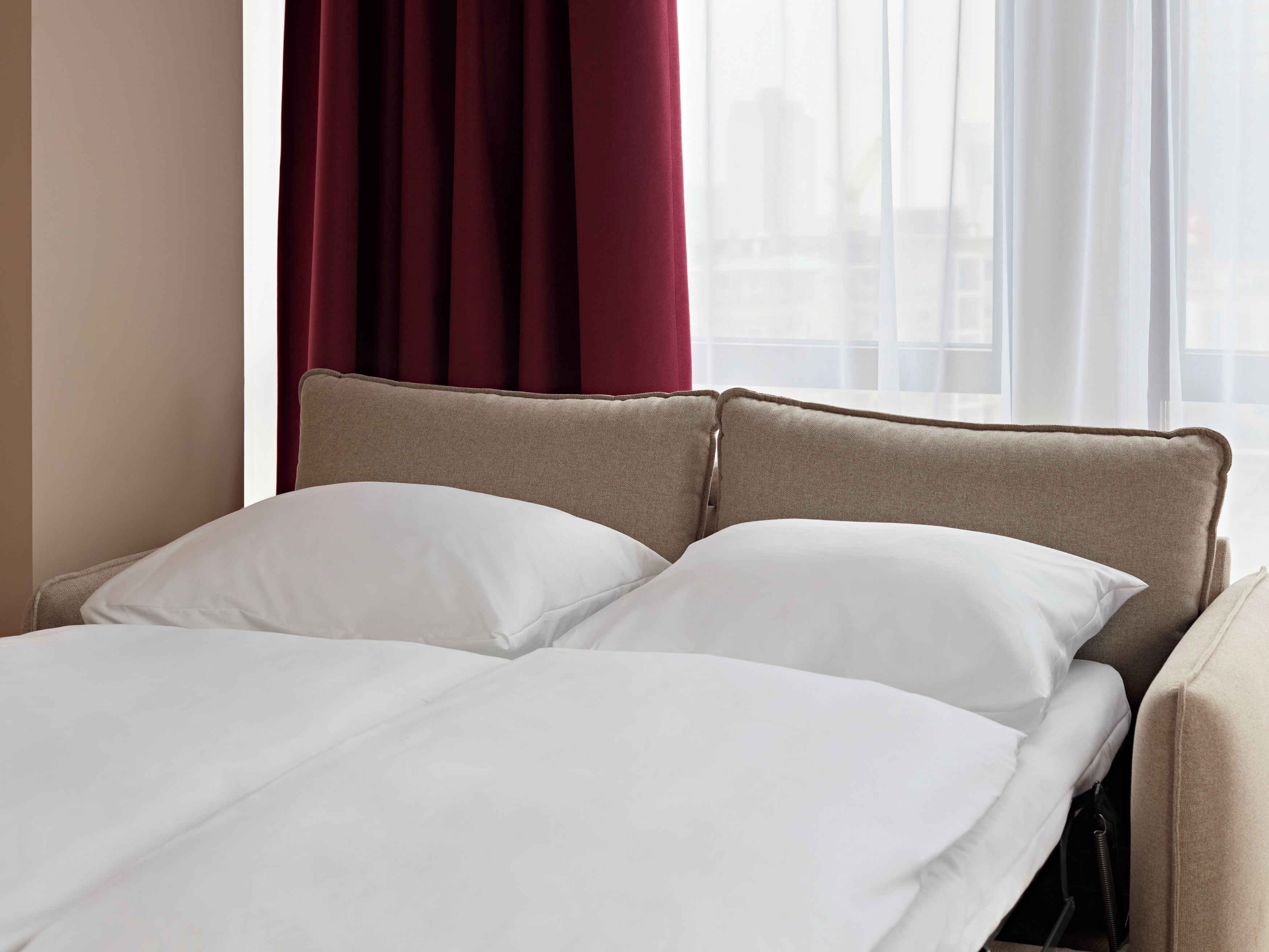 Cama com cabeceira, roupa de cama branca e janela com cortinas.